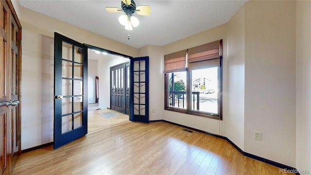 empty room featuring a textured ceiling, french doors, visible vents, and light wood-style floors