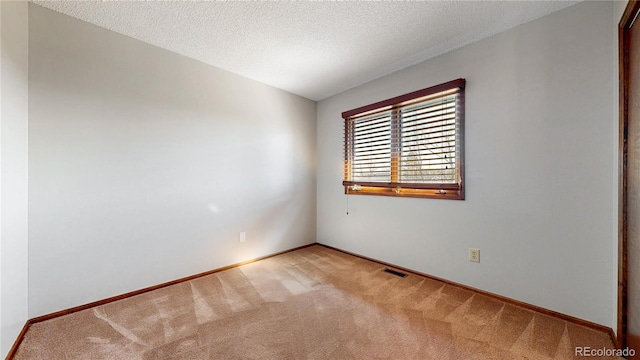 carpeted empty room featuring a textured ceiling, visible vents, and baseboards