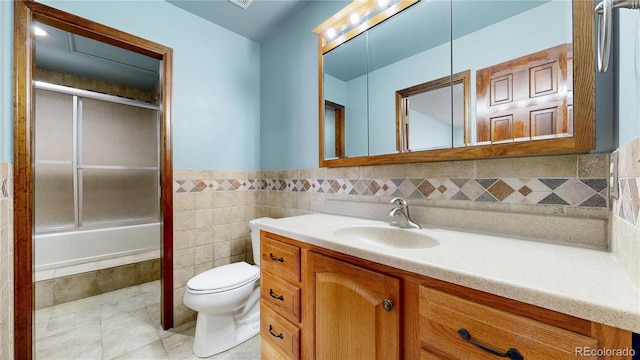 full bathroom with bath / shower combo with glass door, toilet, tile patterned floors, vanity, and tile walls