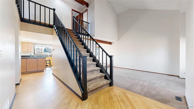 staircase with visible vents, high vaulted ceiling, baseboards, and wood finished floors