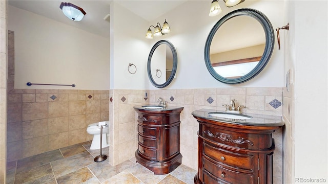 full bath with two vanities, a sink, tile walls, and toilet