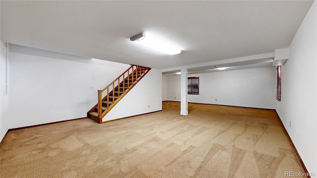 finished below grade area featuring carpet, a textured ceiling, stairway, and baseboards