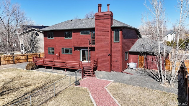 back of house with a deck, a fenced backyard, a shingled roof, a yard, and a chimney