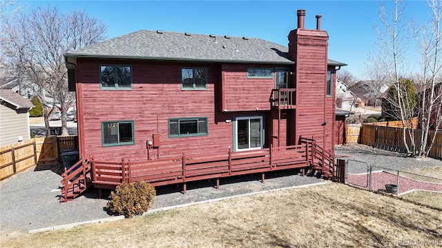 rear view of house featuring a fenced backyard, a shingled roof, a yard, a wooden deck, and a chimney