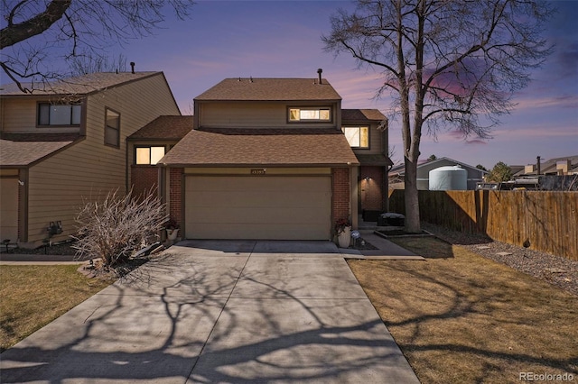 view of front of house featuring a shingled roof, brick siding, concrete driveway, and fence