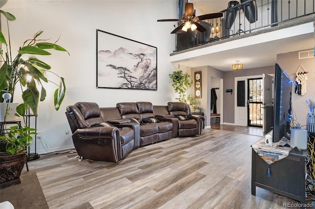 living room featuring visible vents, a ceiling fan, wood finished floors, a high ceiling, and baseboards