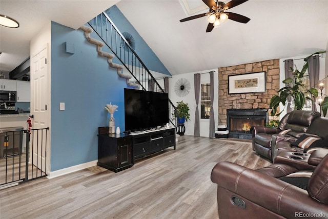 living room with baseboards, ceiling fan, stairway, a stone fireplace, and light wood-style floors