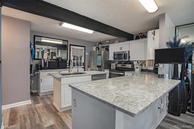 kitchen featuring light wood-style flooring, a center island with sink, a sink, appliances with stainless steel finishes, and a peninsula