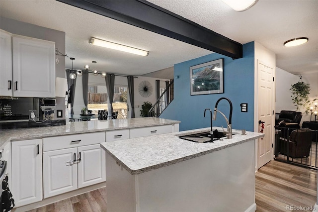 kitchen featuring a center island with sink, a sink, white cabinetry, a peninsula, and light wood finished floors