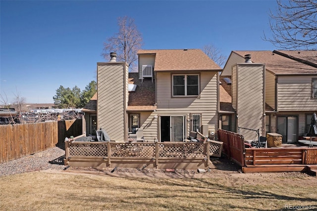 back of property with a chimney, a shingled roof, a deck, and fence