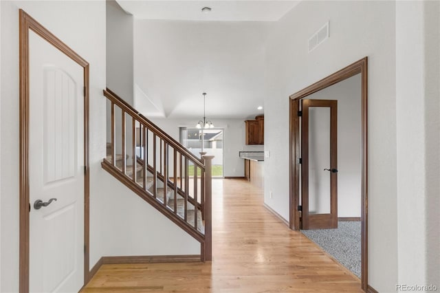 hall with light wood-type flooring, a chandelier, stairway, and baseboards
