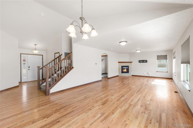 unfurnished living room with light wood-type flooring, stairway, a chandelier, arched walkways, and baseboards