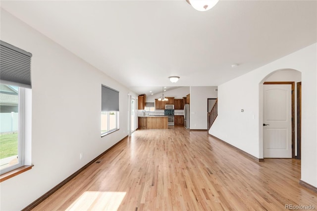unfurnished living room featuring light wood-style floors, arched walkways, stairway, and baseboards