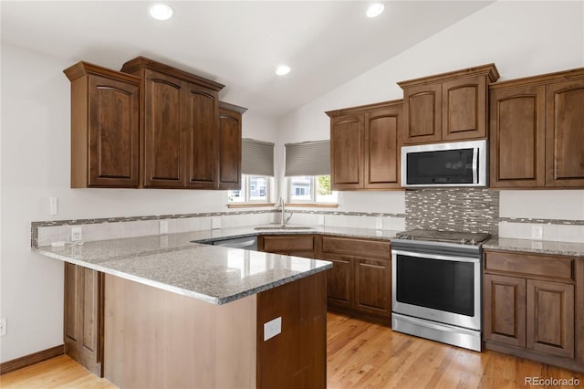 kitchen featuring appliances with stainless steel finishes, a sink, lofted ceiling, a peninsula, and light stone counters