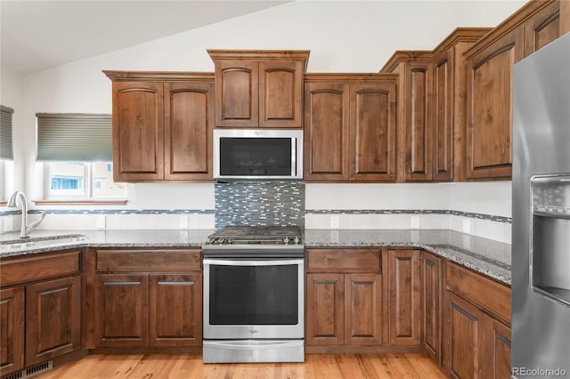 kitchen featuring appliances with stainless steel finishes, a sink, lofted ceiling, light stone counters, and light wood-style floors