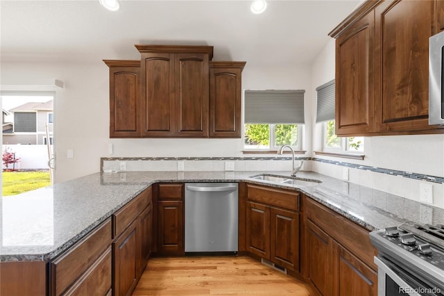 kitchen featuring stainless steel appliances, a sink, light wood-style floors, light stone countertops, and a peninsula