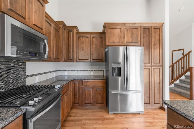 kitchen with appliances with stainless steel finishes, dark stone countertops, and light wood finished floors