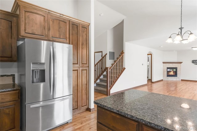 kitchen with stainless steel fridge with ice dispenser, light wood finished floors, a chandelier, arched walkways, and hanging light fixtures