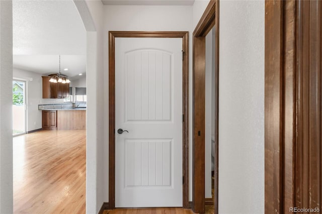 corridor featuring light wood finished floors, arched walkways, and a chandelier