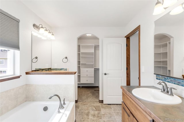 bathroom featuring a walk in closet, a bath, and vanity