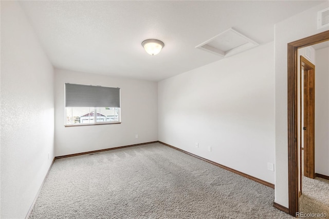 empty room featuring attic access, carpet floors, and baseboards