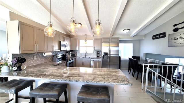 kitchen featuring hanging light fixtures, appliances with stainless steel finishes, a peninsula, and a kitchen bar