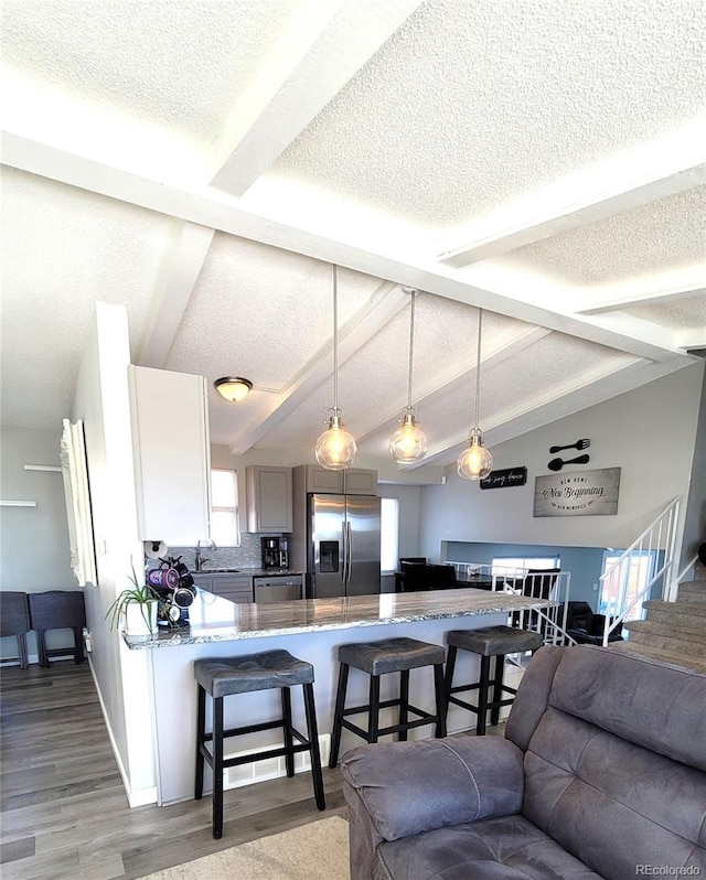 living room featuring vaulted ceiling with beams, light wood-style flooring, baseboards, and a textured ceiling