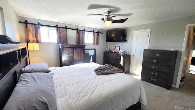 bedroom featuring light carpet, a barn door, a textured ceiling, and a ceiling fan