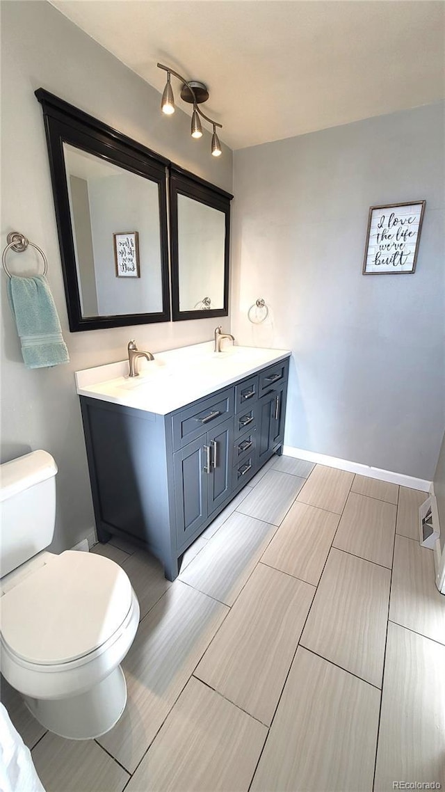 bathroom featuring toilet, a sink, baseboards, double vanity, and track lighting