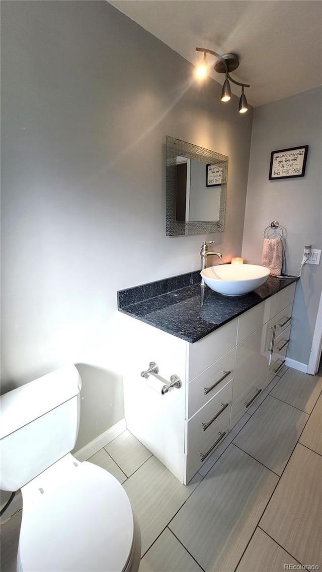 bathroom featuring rail lighting, baseboards, vanity, and toilet