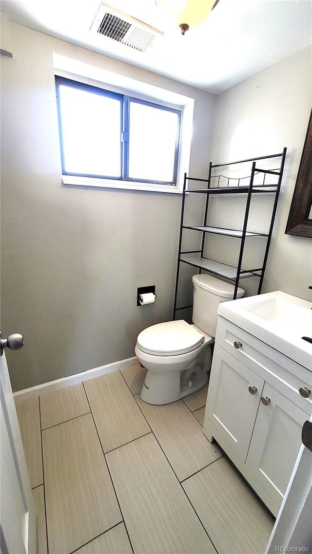 half bath with baseboards, visible vents, vanity, and toilet