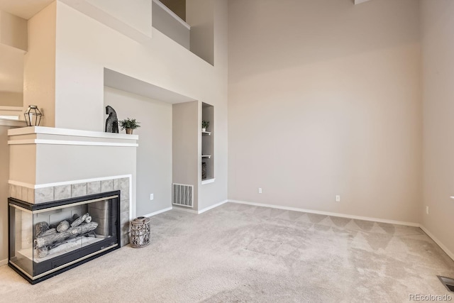 unfurnished living room featuring built in shelves, light colored carpet, a tiled fireplace, and a towering ceiling