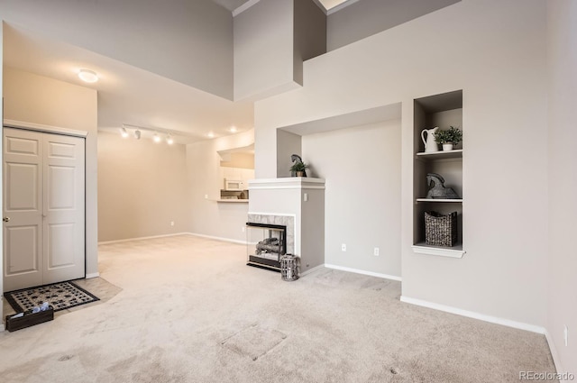 unfurnished living room featuring a tile fireplace, built in features, a high ceiling, carpet, and track lighting