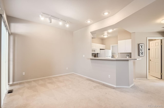 kitchen featuring white appliances, track lighting, white cabinets, light carpet, and kitchen peninsula