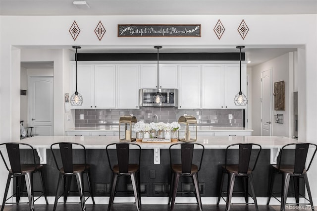 kitchen featuring white cabinets, pendant lighting, decorative backsplash, and a breakfast bar area