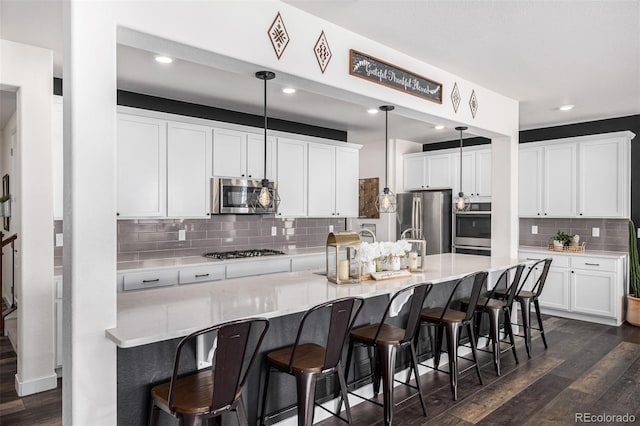 kitchen with white cabinetry, hanging light fixtures, a breakfast bar area, dark hardwood / wood-style floors, and stainless steel appliances