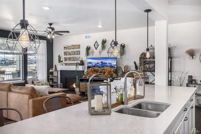 kitchen featuring light stone countertops, decorative light fixtures, ceiling fan, and sink