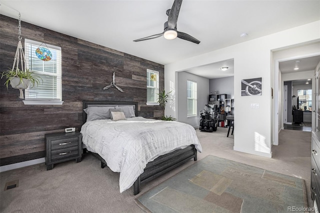 bedroom with wood walls, ceiling fan, and light colored carpet