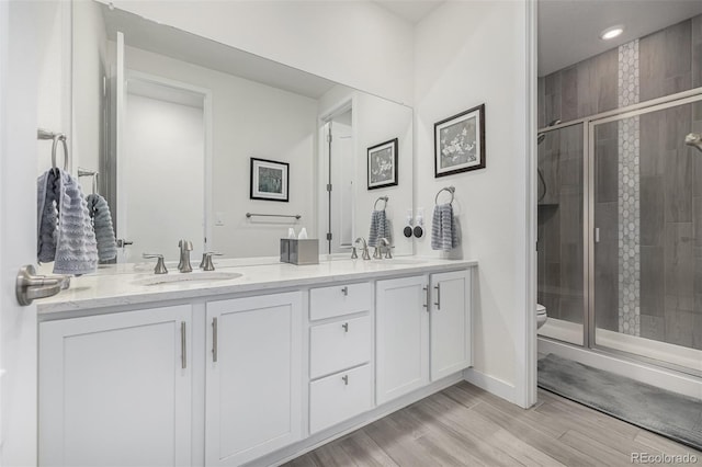 bathroom featuring wood-type flooring, vanity, toilet, and a shower with shower door