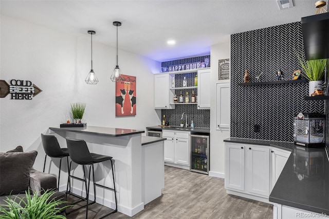 kitchen featuring beverage cooler, a kitchen bar, white cabinets, decorative light fixtures, and kitchen peninsula