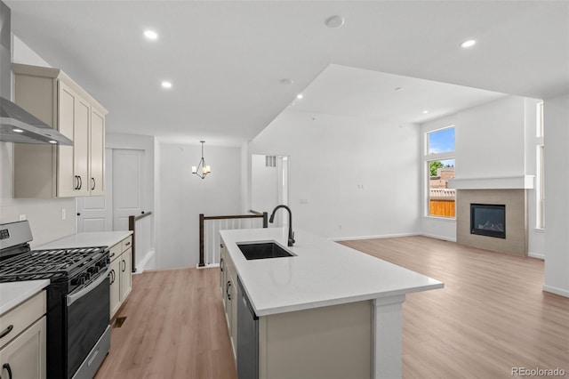11341 W Alder Dr, Littleton, CO 80127 - kitchen with stainless steel appliances, wall chimney exhaust hood, light wood finished floors, a center island with sink, and open floor plan