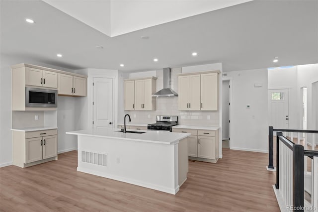 11341 W Alder Dr, Littleton, CO 80127 - kitchen with wall chimney exhaust hood, appliances with stainless steel finishes, tasteful backsplash, a center island with sink, and light wood-style flooring