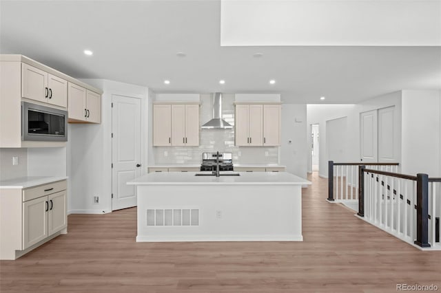 11341 W Alder Dr, Littleton, CO 80127 - kitchen with built in microwave, wall chimney exhaust hood, backsplash, a center island with sink, and light wood finished floors