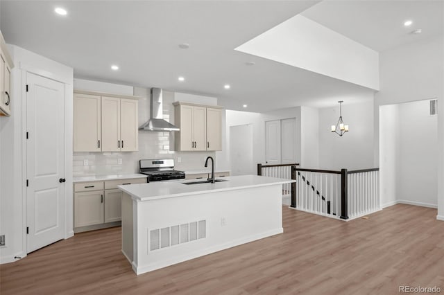 11341 W Alder Dr, Littleton, CO 80127 - kitchen with wall chimney exhaust hood, gas range, light wood-style floors, tasteful backsplash, and a center island with sink
