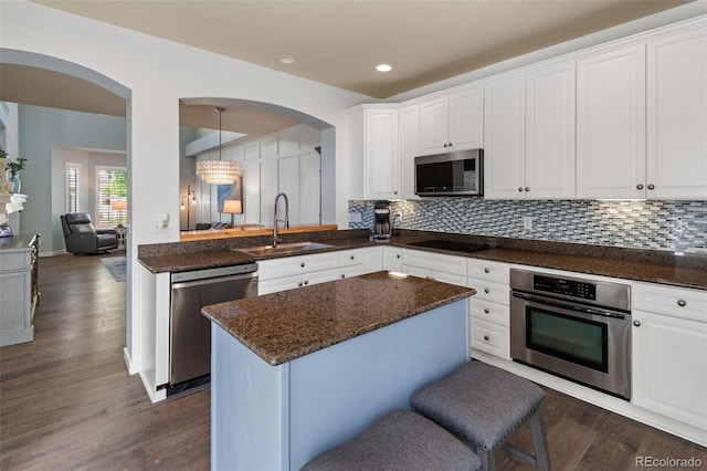 8318 Devinney Ct, Arvada, CO 80005 - kitchen with stainless steel appliances, arched walkways, white cabinets, dark wood finished floors, and recessed lighting