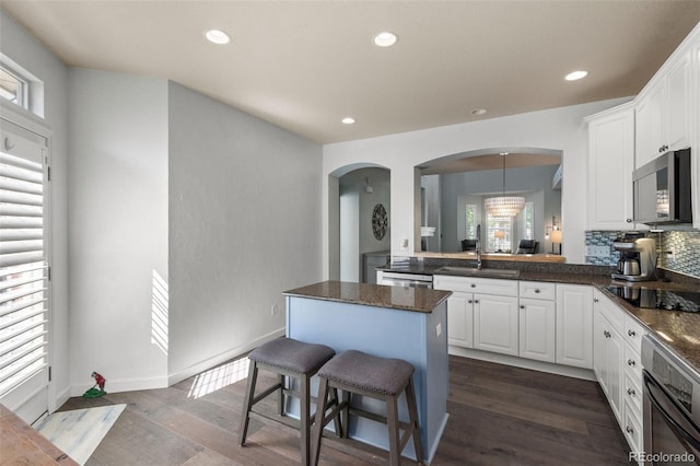8318 Devinney Ct, Arvada, CO 80005 - kitchen with black appliances, arched walkways, white cabinetry, a center island, and a breakfast bar