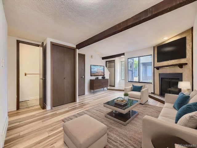 living room featuring a large fireplace, beam ceiling, light hardwood / wood-style floors, and a textured ceiling