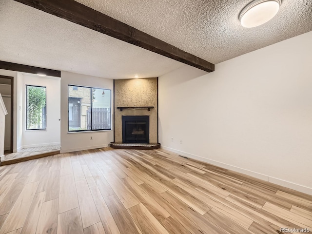 unfurnished living room with beam ceiling, a fireplace, a textured ceiling, and light wood-type flooring