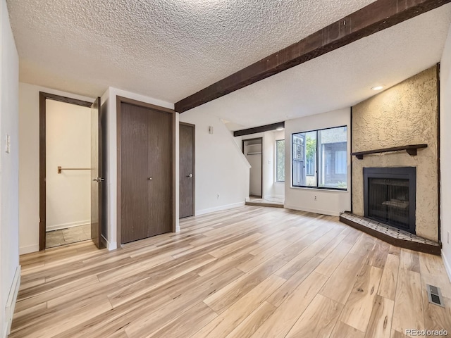 unfurnished living room with beamed ceiling, light hardwood / wood-style floors, and a textured ceiling