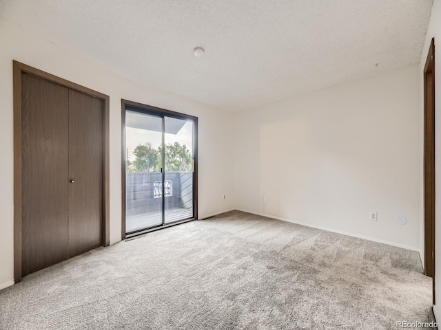 unfurnished bedroom featuring a closet, a textured ceiling, carpet, and access to outside